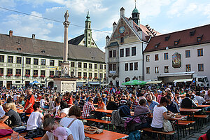 Das Foto zeigt Menschen, die an Biertischen auf dem Marienplatz Freising sitzen während des Altstadtfests