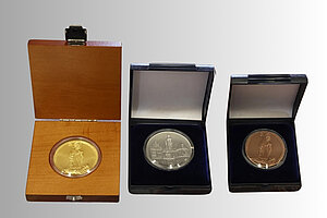 The anniversary medals are available in gold, silver and copper. The obverse depicts Saint Corbinian in Freising with the loaded bear, while the reverse shows Freising's Marienplatz with the town hall, Stauberhaus, St George's parish church and the Marian column.